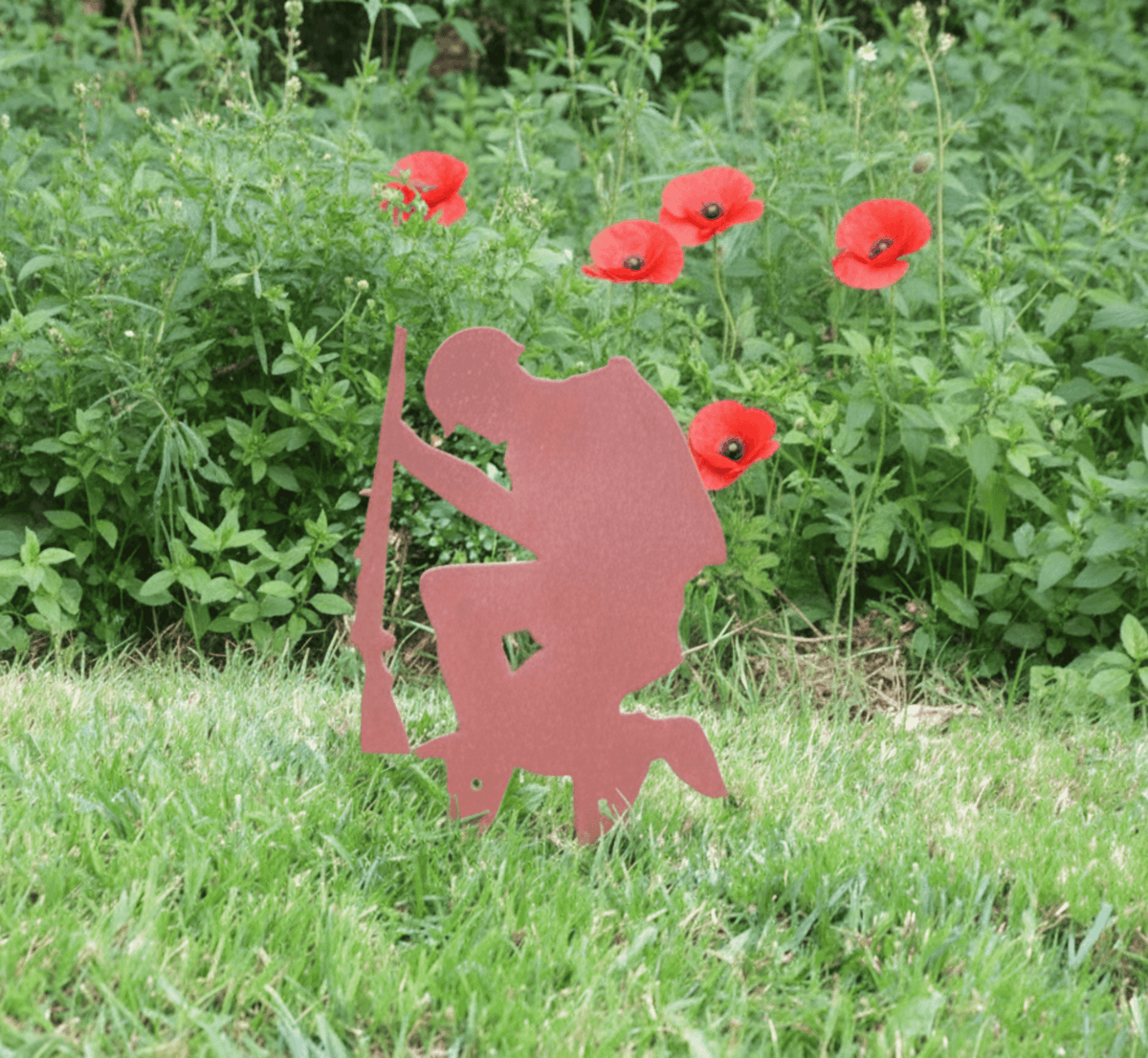 Rustic Steel SOLDIER Garden Ornament displayed in a garden with red poppies, handmade metal military art decoration.