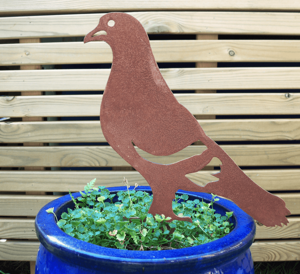 Rusty Steel PIGEON Garden Ornament displayed in a blue pot with greenery, showcasing unique rustic charm.