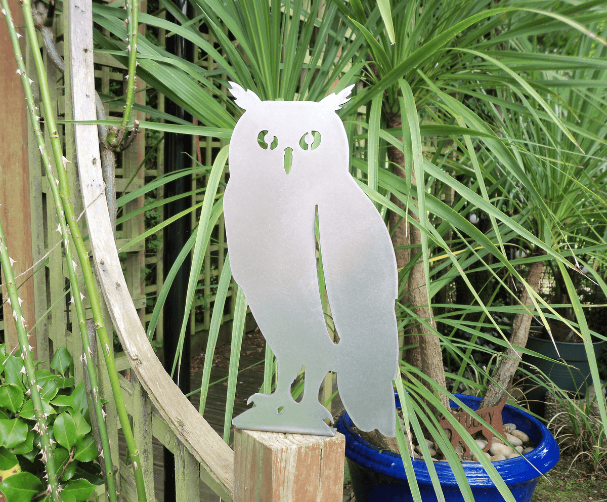 Rustic Steel OWL Garden Ornament standing on a fence post, surrounded by lush greenery in a garden setting.