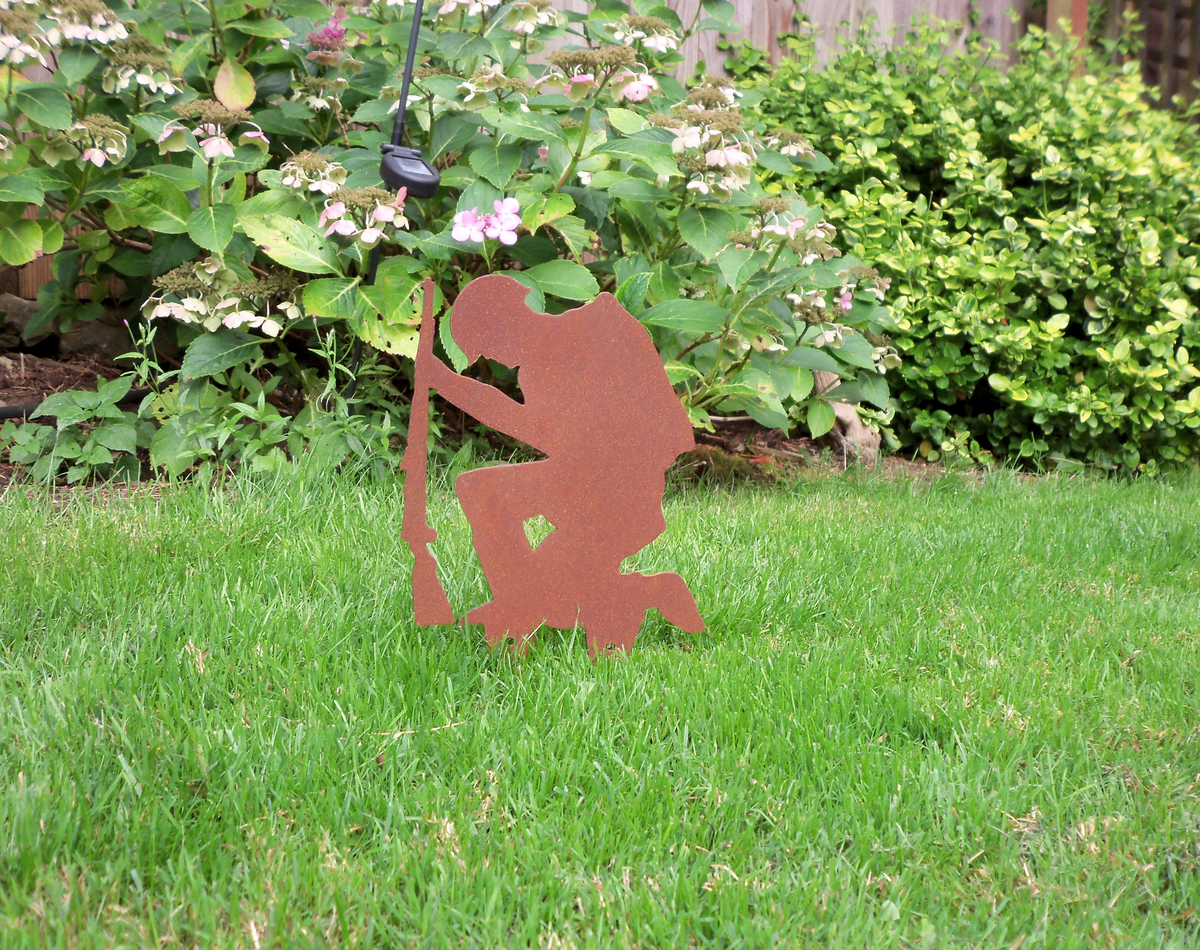 Rustic Steel SOLDIER Garden Ornament shown in garden, depicting a kneeling soldier with rifle against green grass.