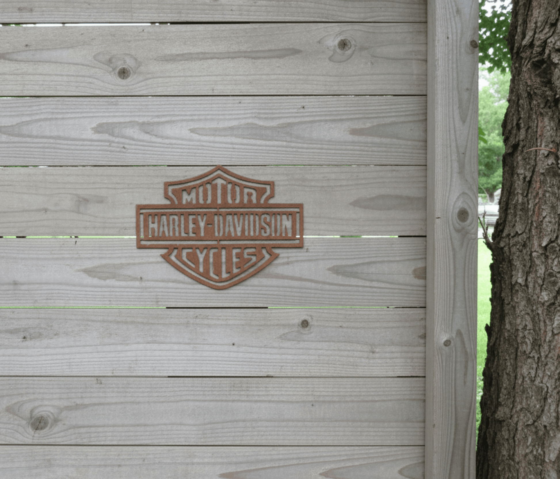 Rustic Metal Harley Davidson Motorcycle Badge Sign on a wooden fence beside a tree