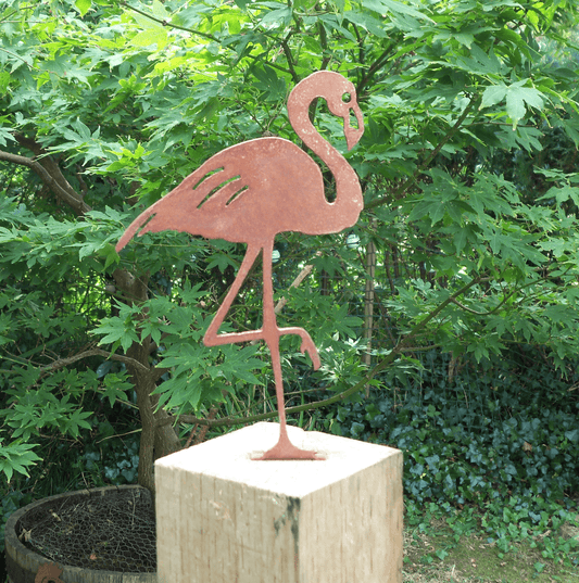 Rusty Metal Flamingo garden ornament standing on a wooden post surrounded by green foliage.