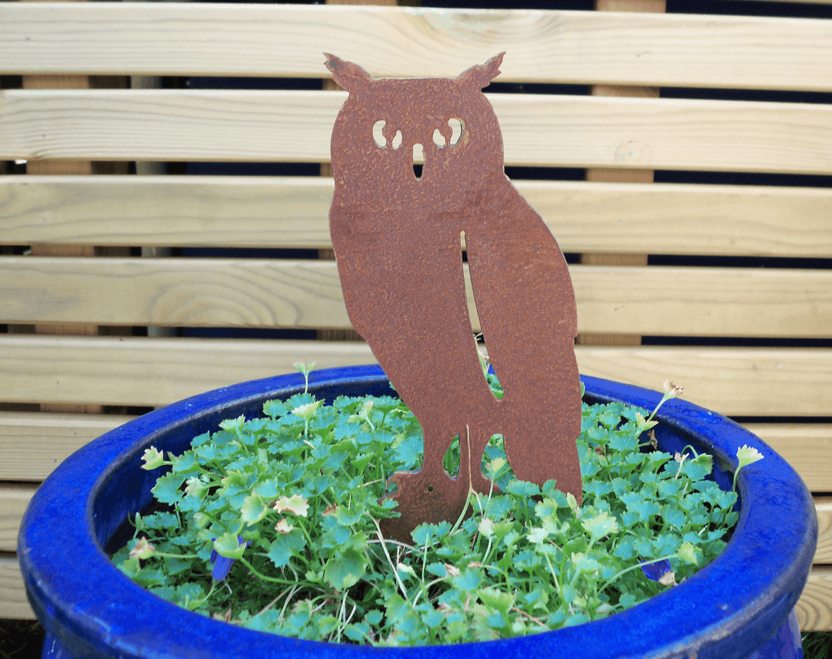 Rusted Steel Owl Garden Ornament displayed in a blue pot with green plants, adding rustic charm to outdoor decor.