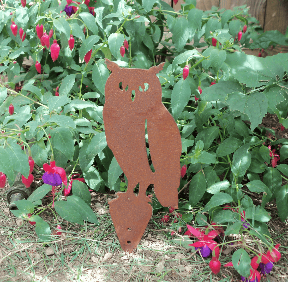 Handmade rusted steel owl garden ornament among blooming flowers, perfect for enhancing garden decor.