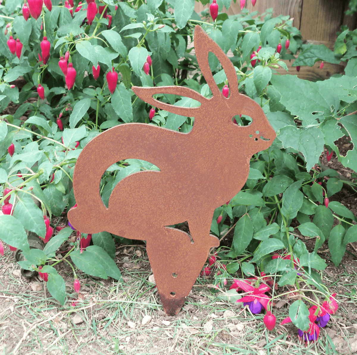Rusted Steel RABBIT Garden Ornament among flowering plants, showcasing unique rusted finish and industrial charm.