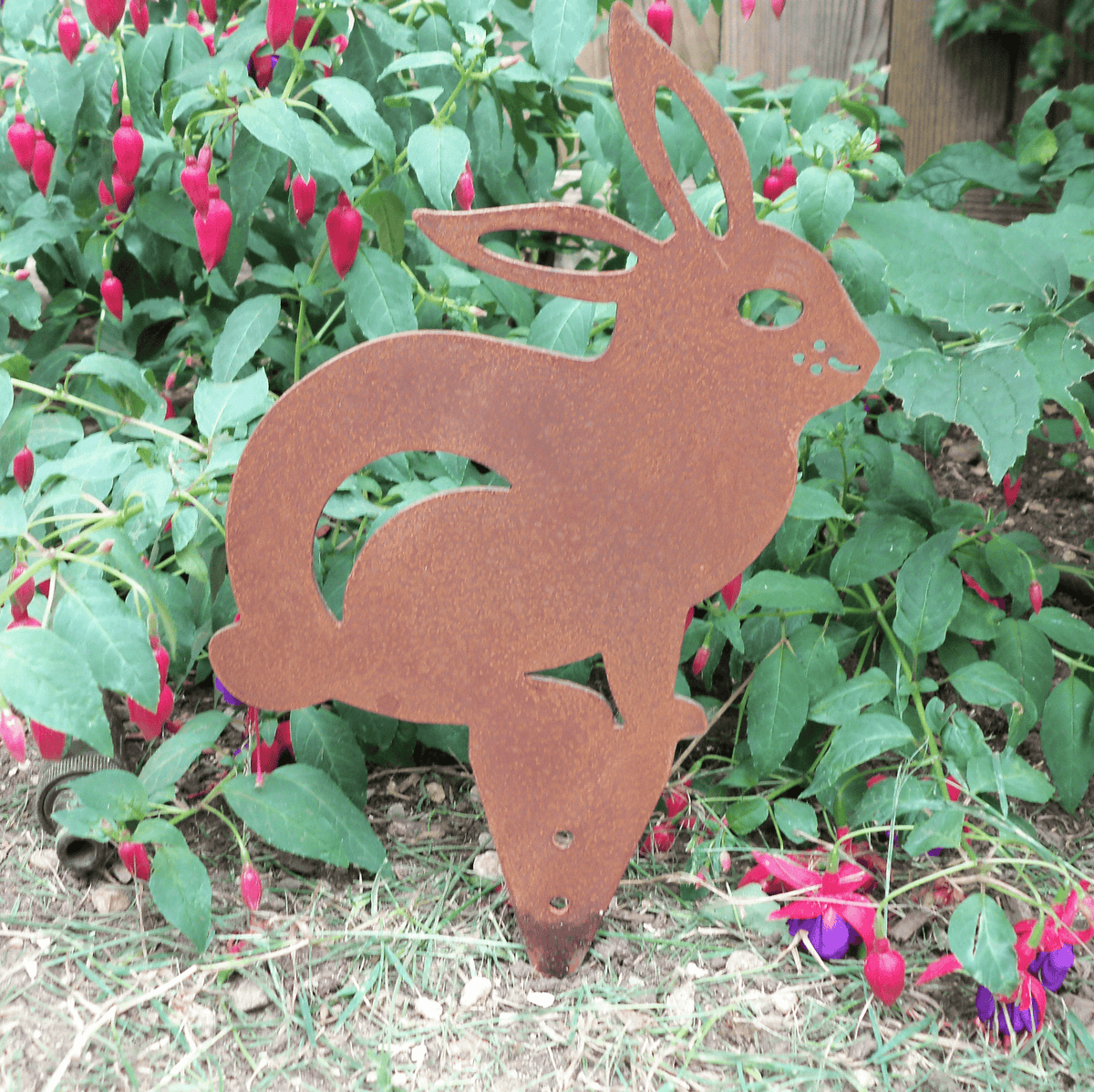 Rusted Steel RABBIT Garden Ornament in natural setting with flowers, a unique rustic metal animal decoration.