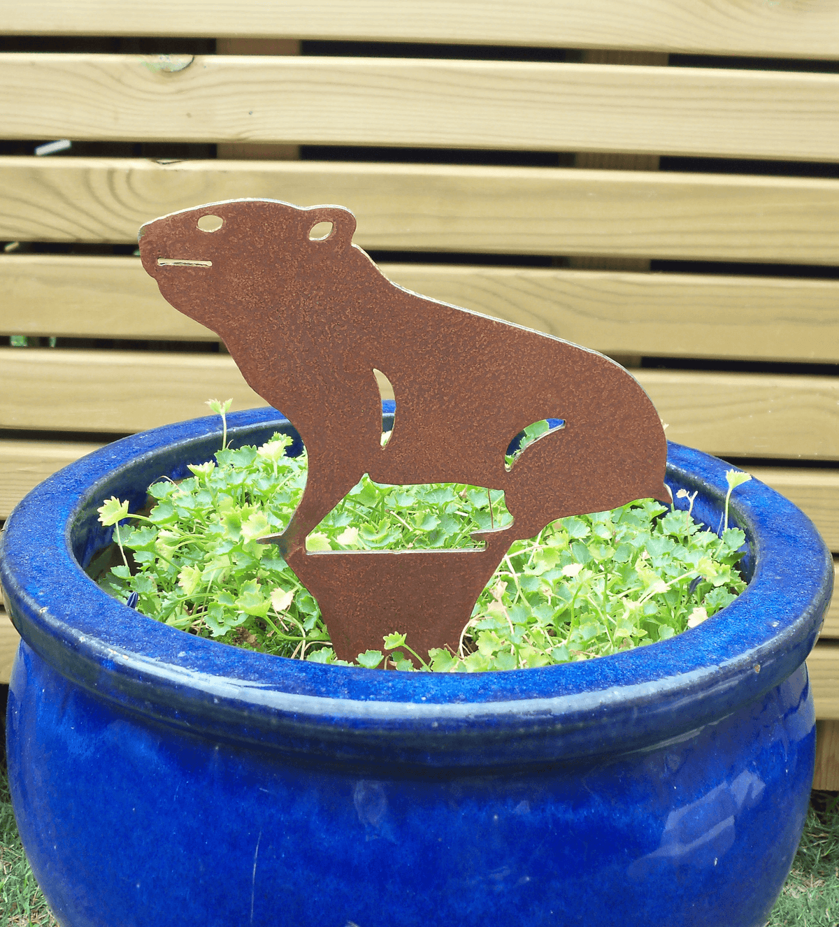 Rusty Steel HAMSTER Garden Ornament displayed in a blue pot filled with green plants, adding rustic charm to the garden.
