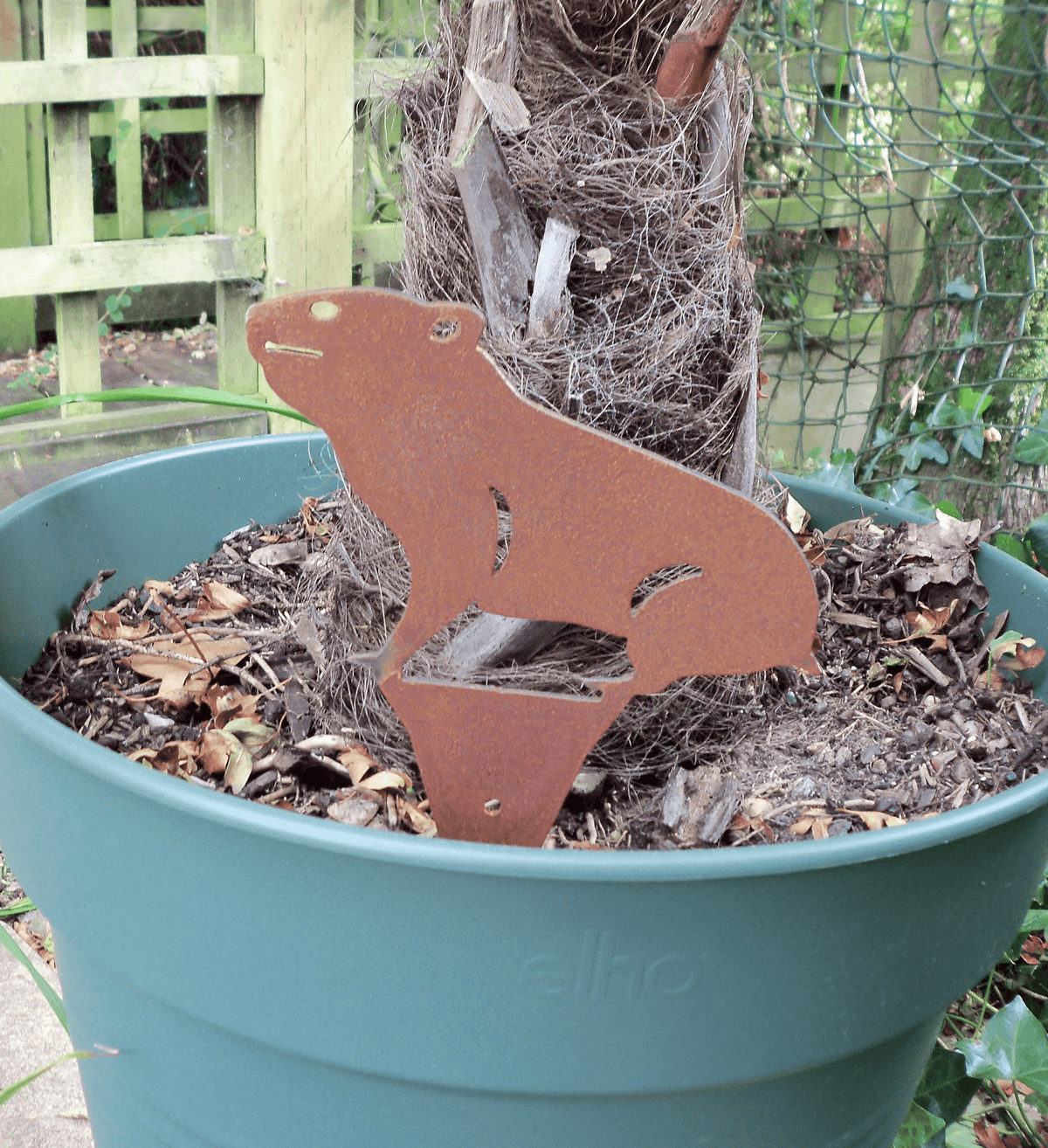 Rusty Steel HAMSTER Garden Ornament displayed in a green planter, adding rustic charm to outdoor space.