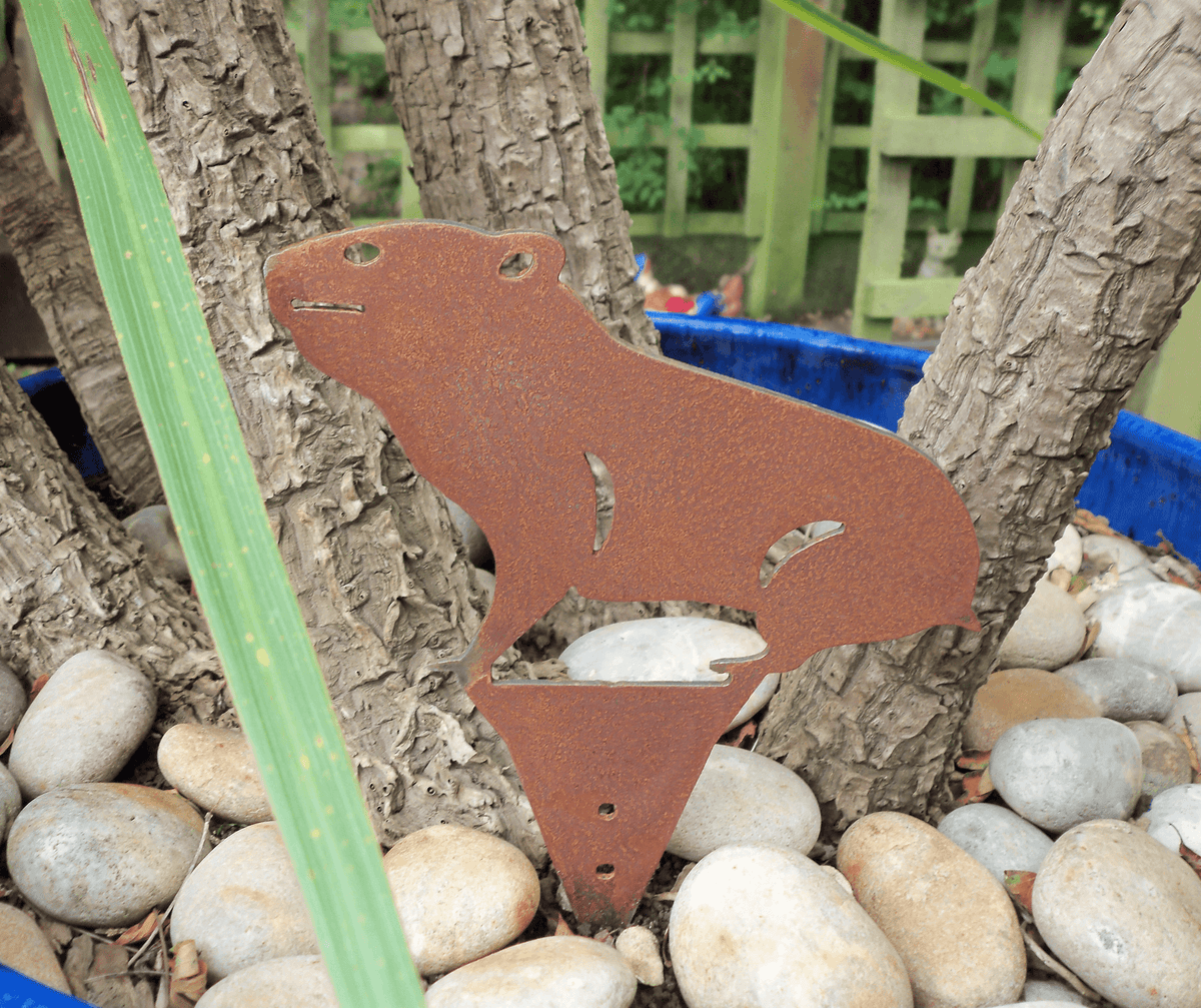Rusty Steel HAMSTER Garden Ornament in a garden setting, adding rustic charm by a tree and rocks.