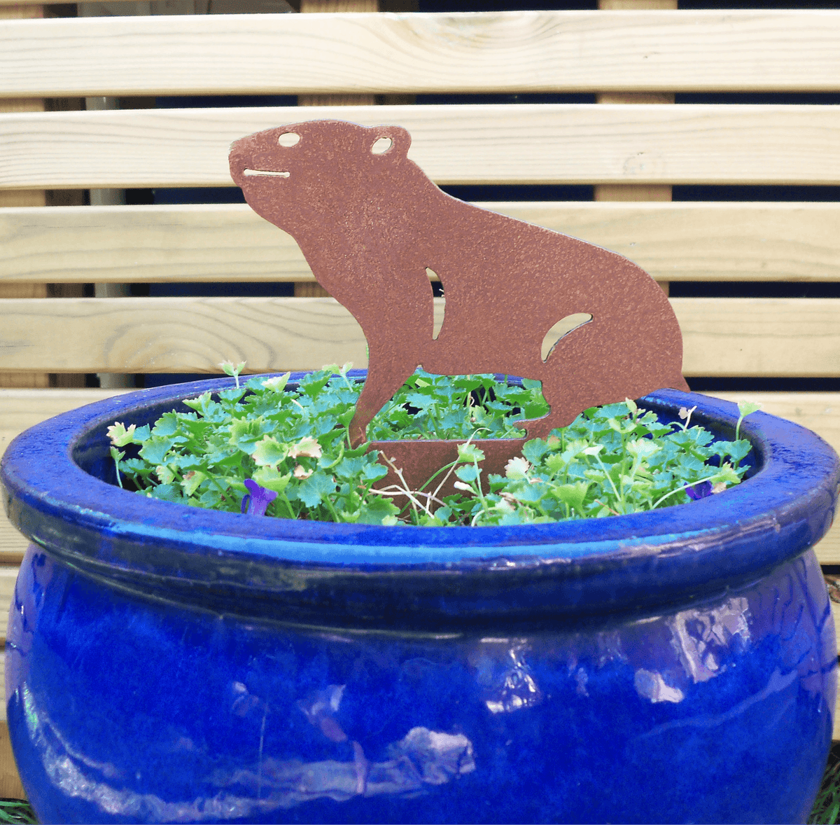 Rusty Steel HAMSTER Garden Ornament placed in a blue pot with greenery, adding rustic charm to the garden.