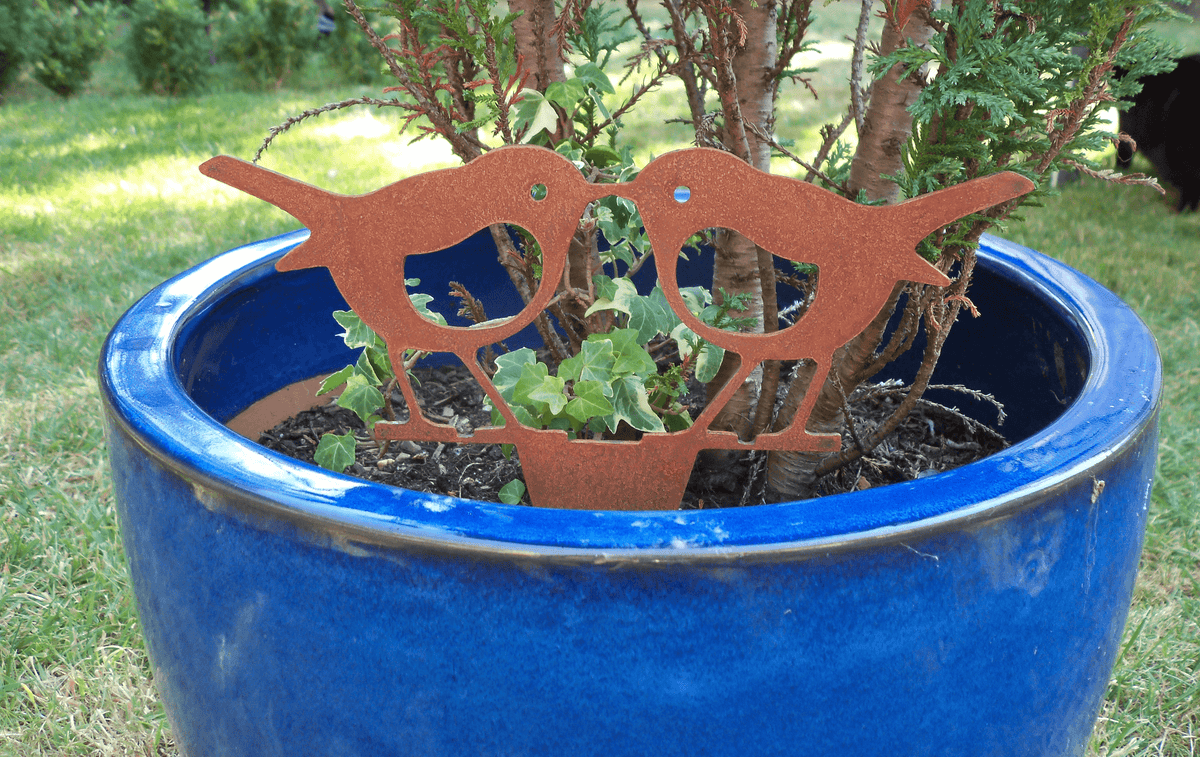 rusty steel kissing robins garden ornament in a blue pot with plants, adding rustic charm to the garden.