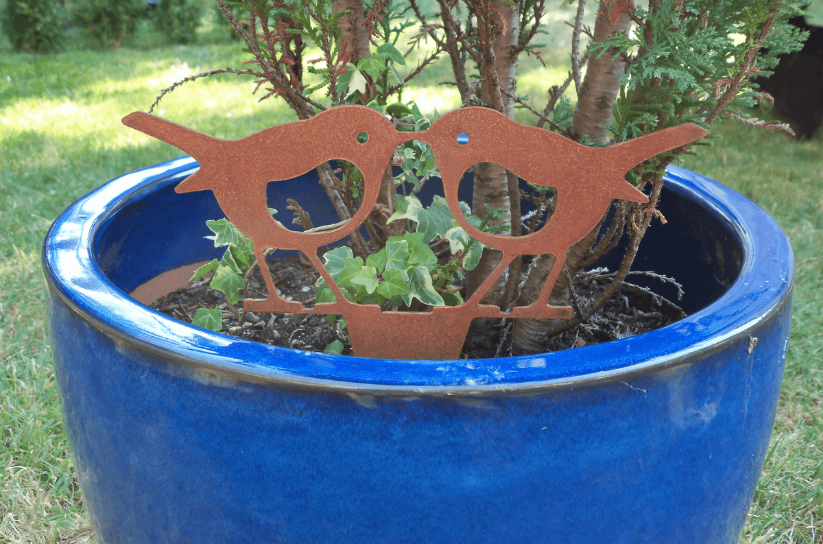 Rusty steel kissing robins garden ornament in a blue planter, adding rustic charm to garden decor.